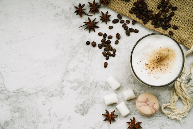 Overhead view of coffee cup with star anise; coffee beans; marshmallow and macaroon