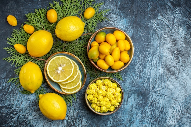 Overhead view of collection of cut and whole natural organic fresh citrus fruits on fir branches and a pot with candies on dark background