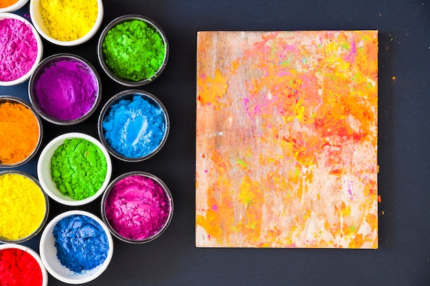 An overhead view of color powder near wooden board on black backdrop