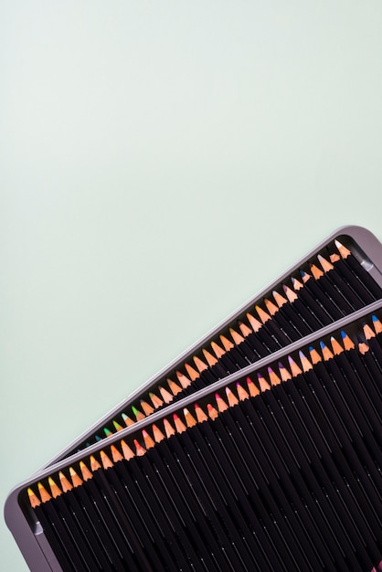 An overhead view of colored pencils on an open metal box against gray background