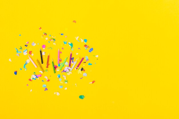 Overhead view of colorful candles with confetti on yellow background