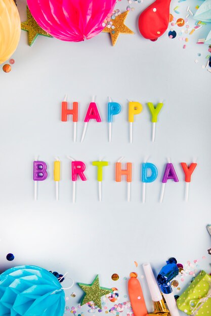 An overhead view of colorful happy birthday candles with party items on white backdrop