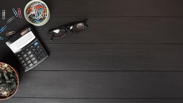 カラフルな紙クリップのオーバーヘッドビュー。黒の木製のテーブル上の電卓と眼鏡