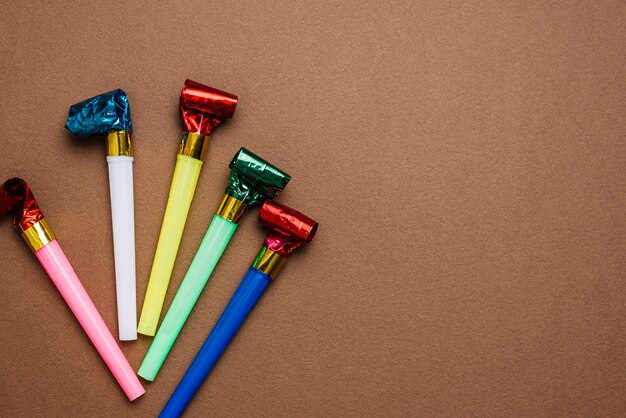 An overhead view of colorful party horn blowers on brown background