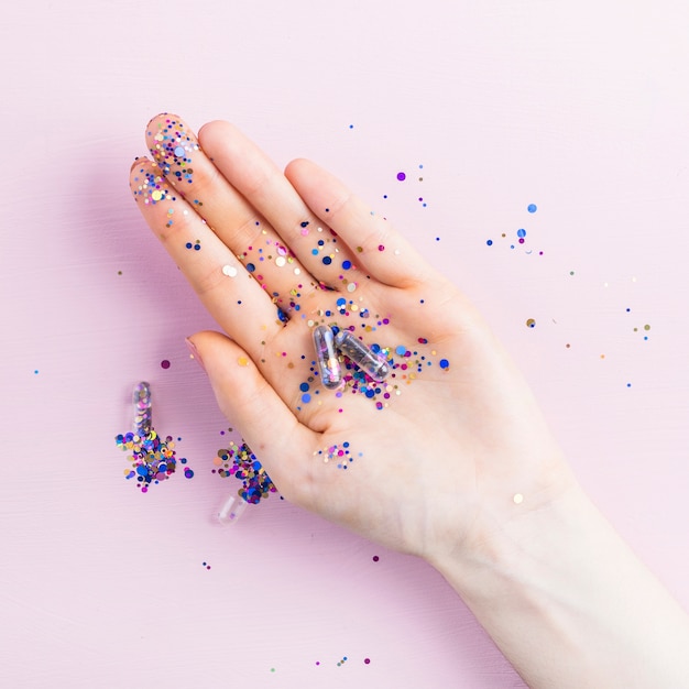 Overhead view of colorful transparent sequin capsule in hand over pink background