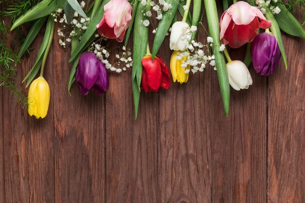 An overhead view of colorful tulips and baby's breath flower on wooden desk