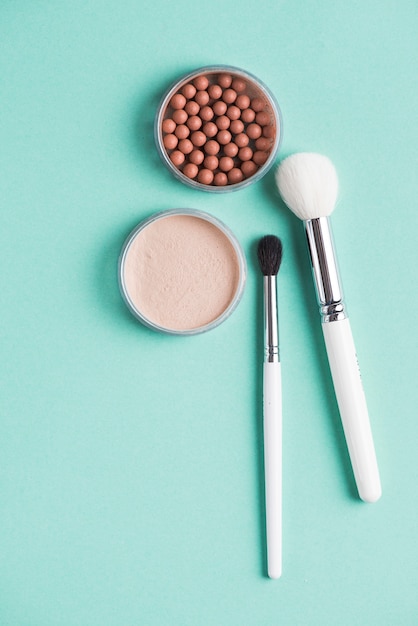 An overhead view of compact and bronzed pearls with makeup brushes