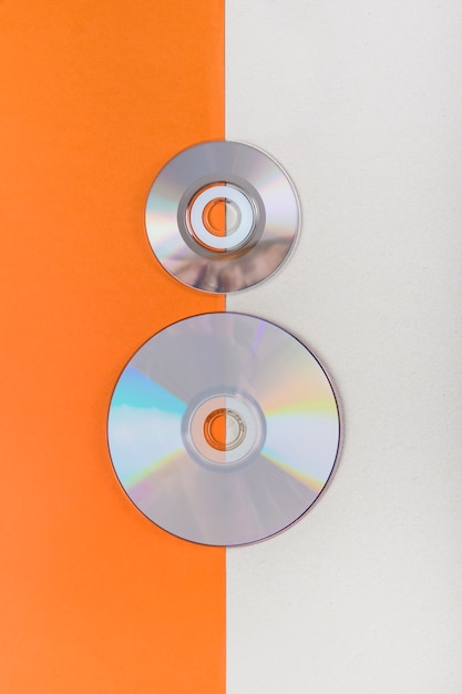 Free photo an overhead view of compact discs on an orange and white dual background