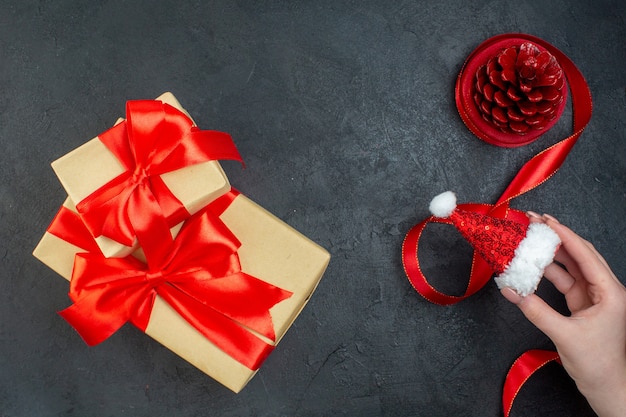 Overhead view of conifer cone and beautiful gift hand holding santa claus hat on dark background