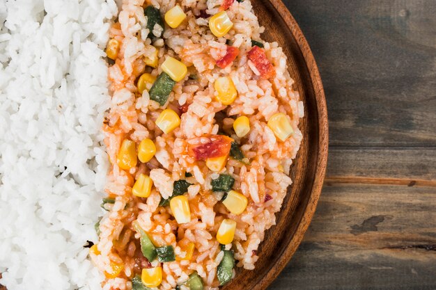 An overhead view of cooked white rice and chinese fried rice with vegetables on wooden tray