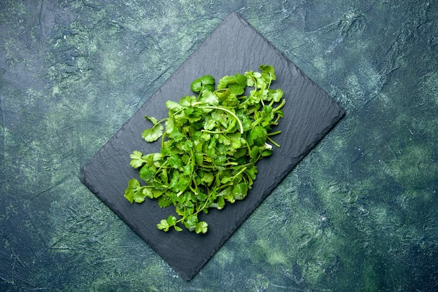 Overhead view of coriander bundle on wooden cutting board on green black mixed colors background with free space