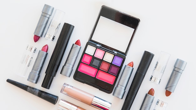 An overhead view of cosmetic eye shadows; different shades of lipstick; and brush on white background