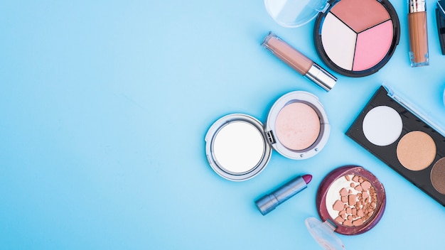 An overhead view of cosmetic face powder; lipstick; and foundation on blue backdrop