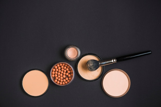 Overhead view of cosmetic products and makeup brush on black background