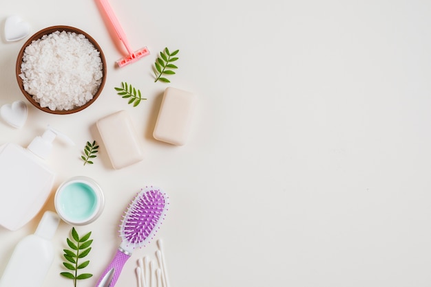 An overhead view of cosmetics products; soap; razor ear buds and green leaves on white backdrop