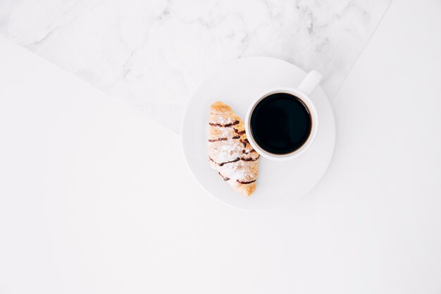 An overhead view of croissant and coffee cup on white plate against textured backdrop