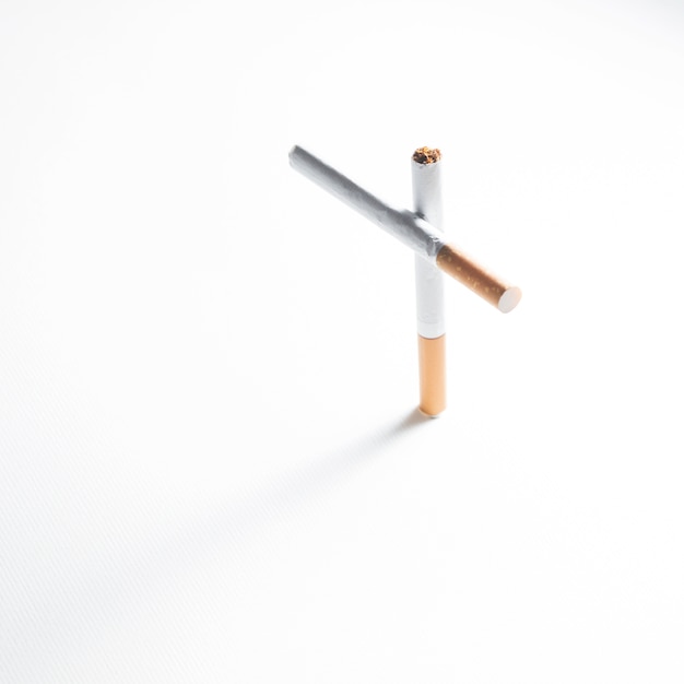 Overhead view of cross sign made from cigarette on white background