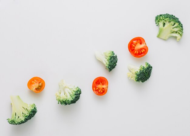 An overhead view of crossed broccoli and halved cherry tomatoes on white background