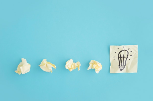 Free photo overhead view of crumpled papers with light bulb draw on the sticky note over the blue background