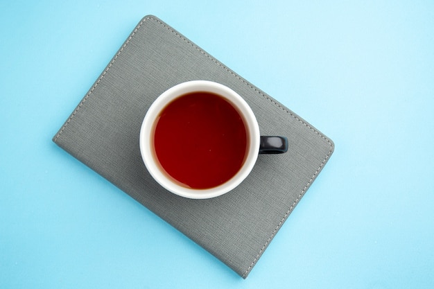 Free photo overhead view of a cup of black tea on gray notebook on blue surface