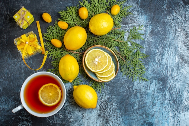 Overhead view of a cup of black tea with lemon and collection of half whole citrus fruits on fir branches gift boxes on dark background