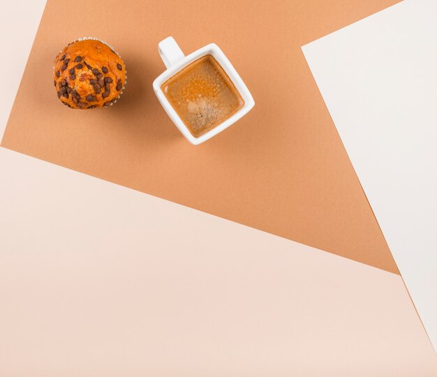 An overhead view of cup cakes and coffee cup on beige dual backdrop