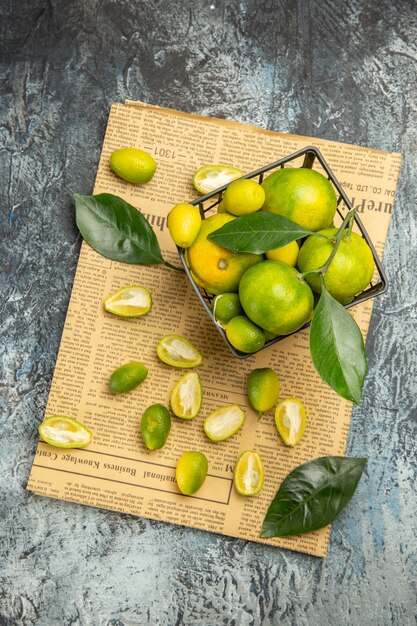 Overhead view of cut in half fresh kumquats and lemons in a black basket on newspapers on gray background stock image