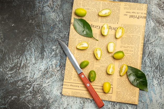 Free photo overhead view of cut in half fresh kumquats on newspapers on gray background