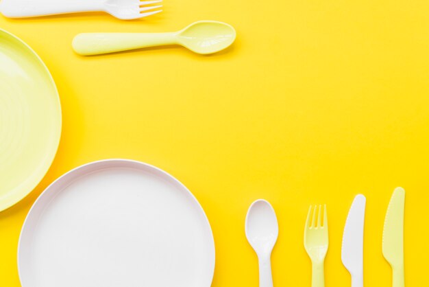 Overhead view of cutlery; plates on yellow background