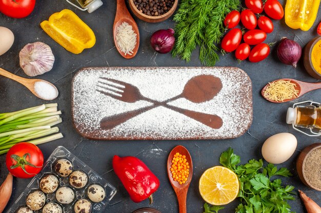 Overhead view of cutting board with flour drawn fork knife among fresh vegetables different spices