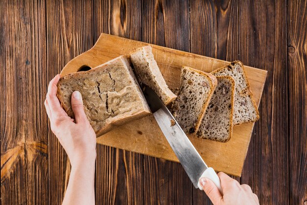 Overhead view of cutting bread with sharp knife on wooden board