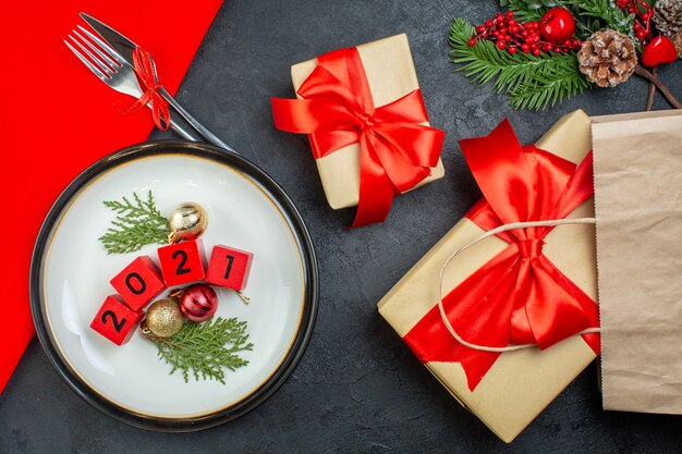 Overhead view of decoration accessories numbers on a plate and beautiful gifts fir branches conifer cone on a dark table