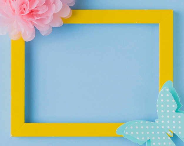 Free photo overhead view of decorative yellow photo frame with flower and butterfly cutout