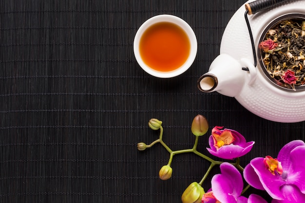 Overhead view of delicate pink orchid flower and dry tea herb with teapot