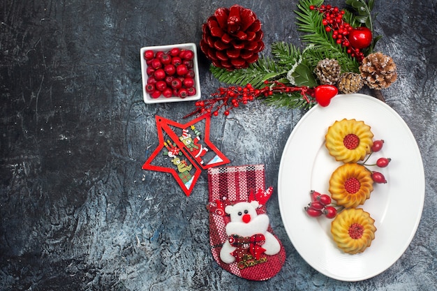 Overhead view of delicious biscuits on a white plate and cornell in a bowl fir branches on dark surface