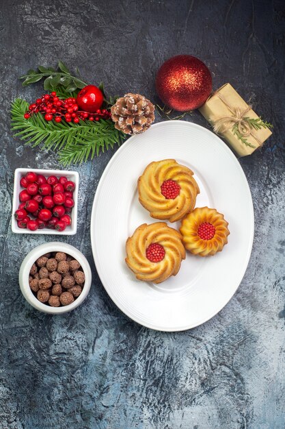 Overhead view of delicious biscuits on a white plate and new year decorations gift cornel in small pot chocolate on dark surface