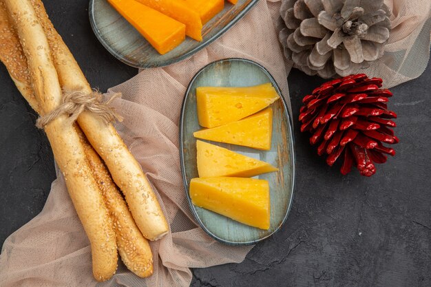 Overhead view of delicious chees slices and conifer cones on a towel on a black background