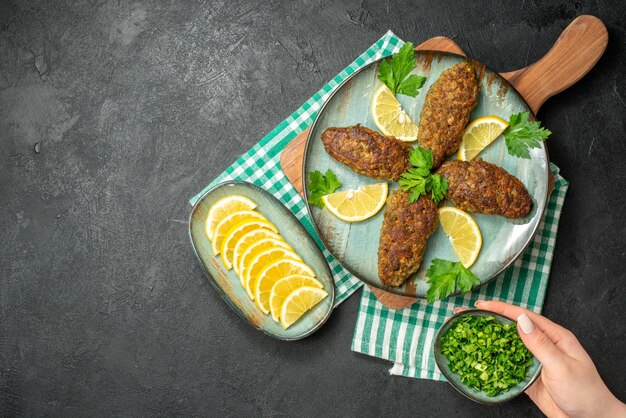 Overhead view of delicious cutlets served with lemon and green on wooden cutting board on yellow stripped towel on black background