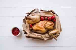 Foto gratuita vista dall'alto del delizioso pollo alla griglia in carta marrone con salsa di pomodoro sul tavolo in legno
