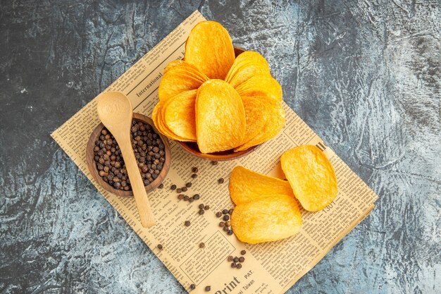 Overhead view of delicious homemade chips and pepper bowl with spoon on newspaper on gray table