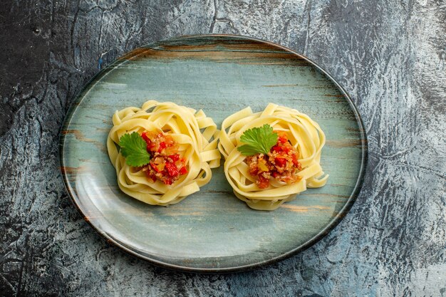 Вид сверху вкусной пасты с томатным мясом и зеленью на синей тарелке на фоне льда