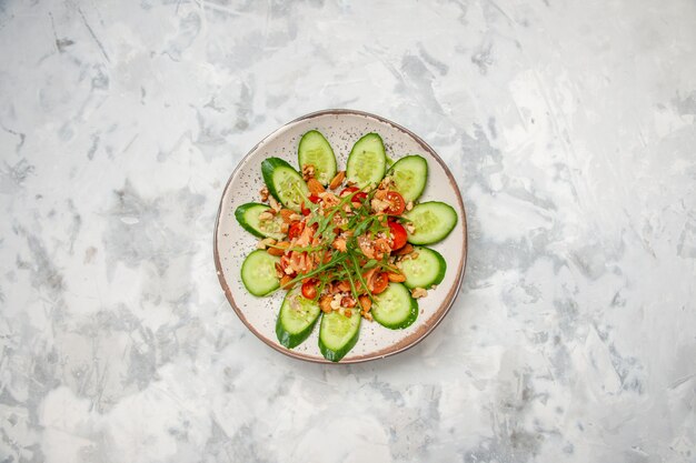 Overhead view of delicious salad decorated with chopped cucumber and greens on stained white surface with free space