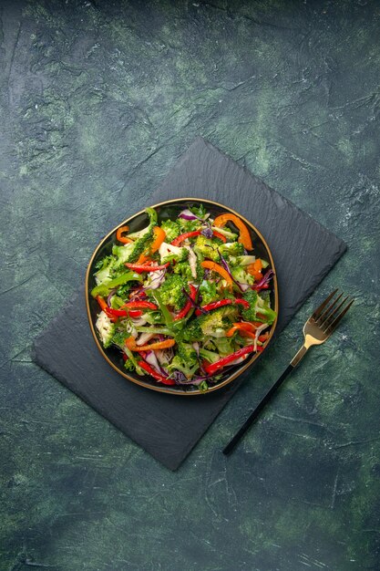 Overhead view of delicious vegetable salad with various ingredients on black cutting board on dark background