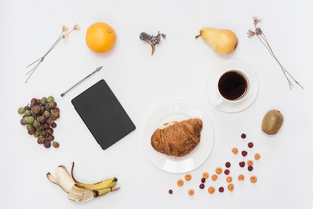 An overhead view of diary and pen with fruits; coffee and croissant isolated on white background