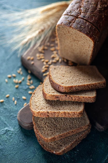 Free photo overhead view of dietary black bread spikes wheats on wooden cutting board on blue dark colors background