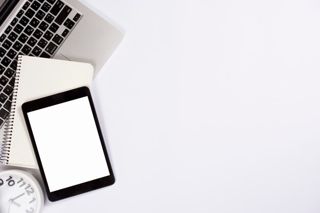 An overhead view of digital tablet; notepad on laptop with alarm clock isolated on white background