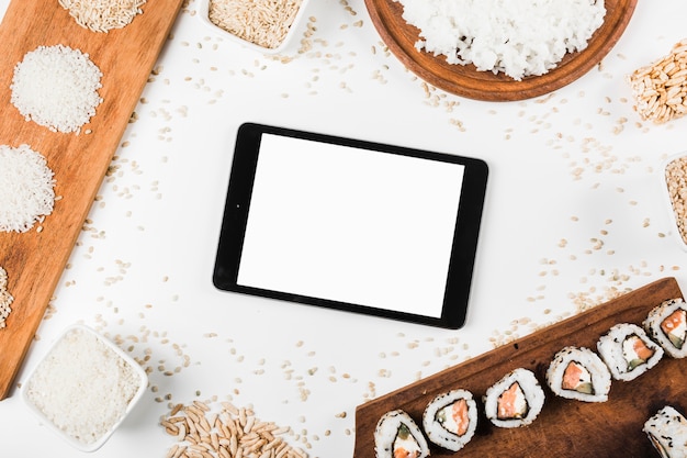 An overhead view of digital tablet surrounded with sushi and variety of uncooked rice