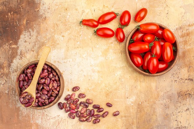 Overhead view of dinner background with beans inside and outside of brown pot with spoon and tomatoes on mixed color background