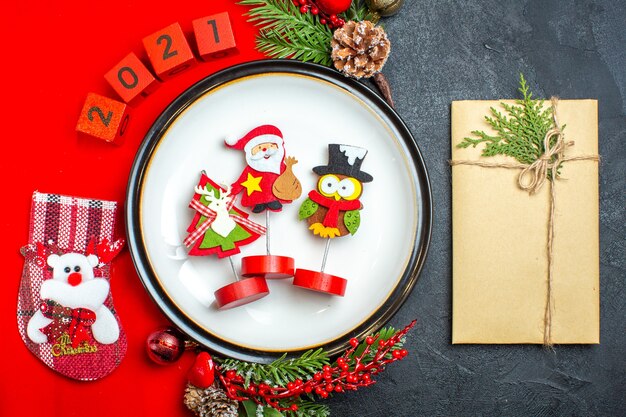 黒いテーブルの上の贈り物の横にある赤いナプキンのディナープレート装飾アクセサリーモミの枝と番号のクリスマスソックスの俯瞰図