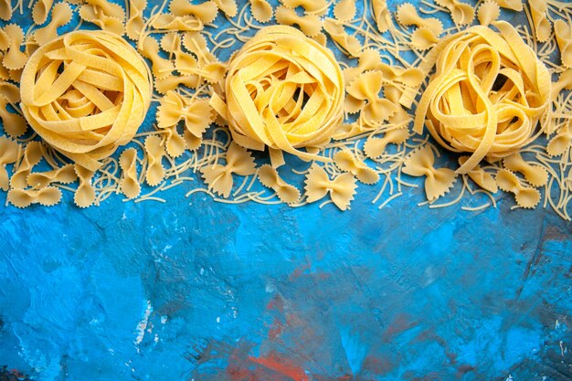 Overhead view of dinner preparation with pasta noodles lined up in a row on blue background